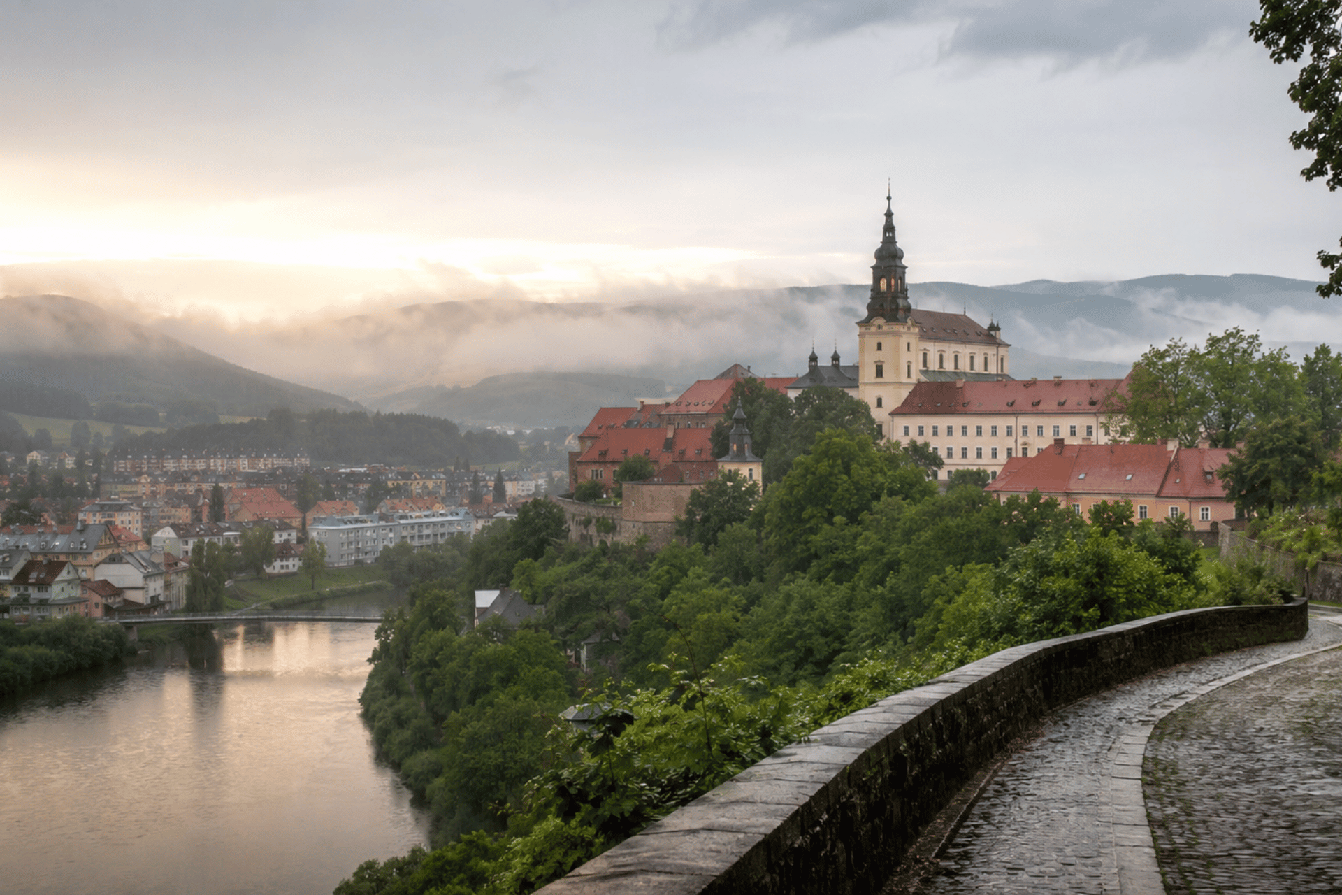 Deštivý pohled na Klášterec nad Ohří se zámkem, řekou Ohří a mlhou nad Krušnými horami